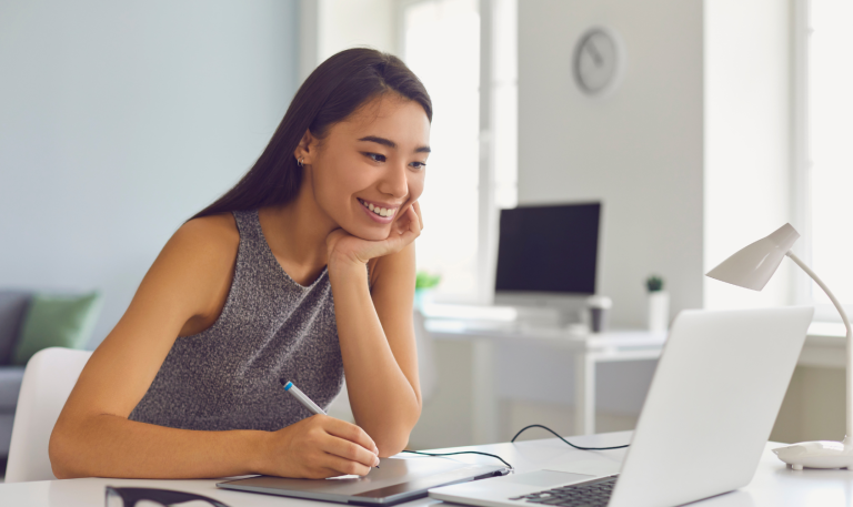 Woman happily reading something on computer and taking notes