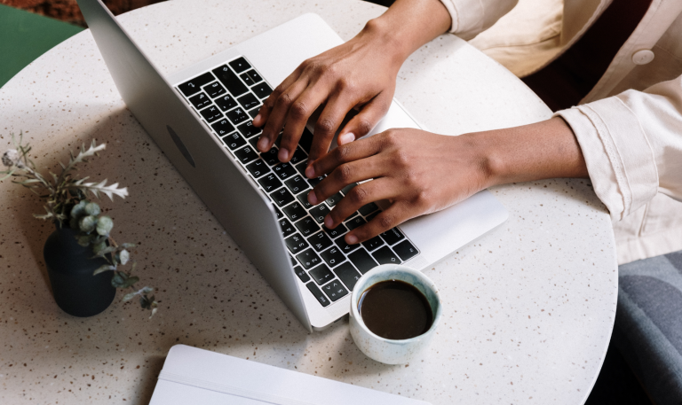 Hands typing on laptop, with plant and coffee also on desk